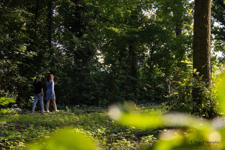Twee personen wandelen door een groen, bosachtig gebied.