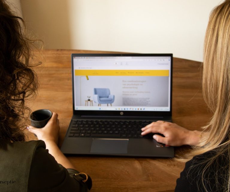 Twee mensen bekijken de ACT en Adem website op een laptop terwijl ze aan een houten tafel zitten.