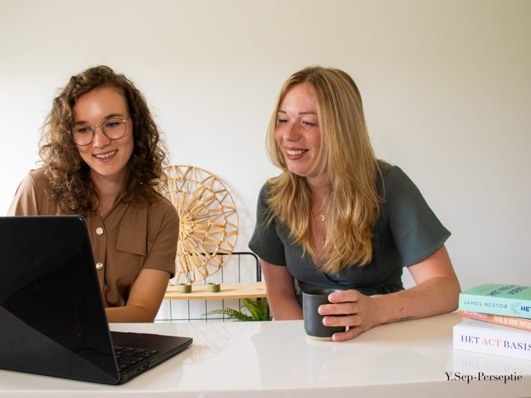 Twee mensen bekijken samen een laptop, de een met een kopje in de hand.